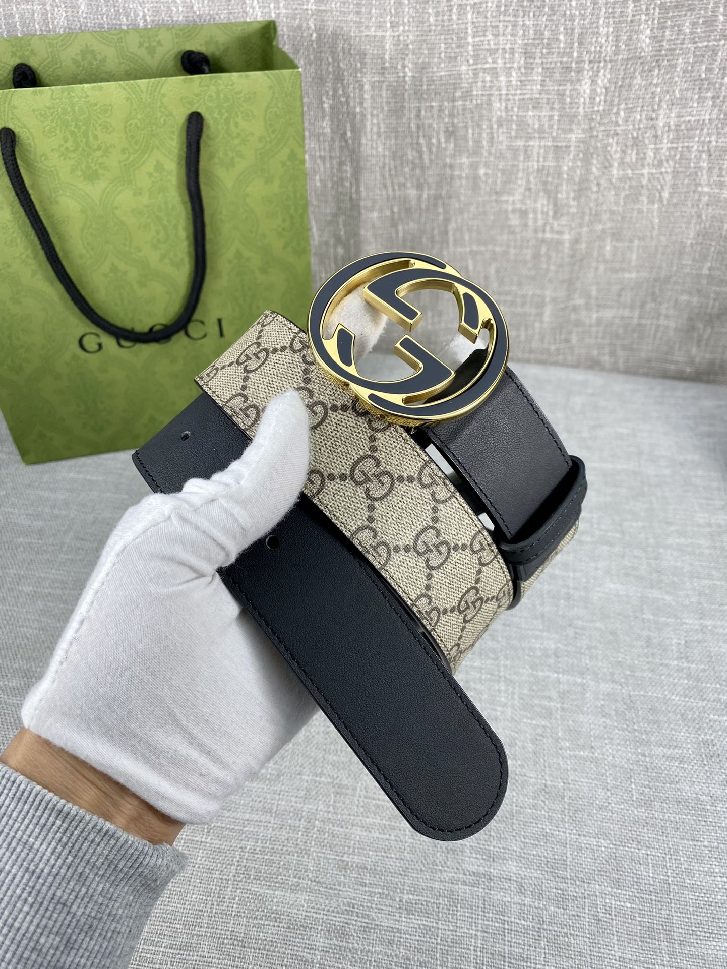 Gucci belt with dark strap and round GG logo buckle, held by gloved hand
