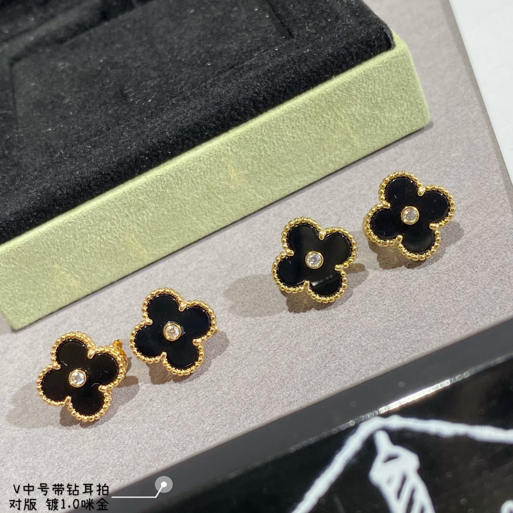 Clover-shaped stud earrings set with gold-tone outlines in black on a display tray
