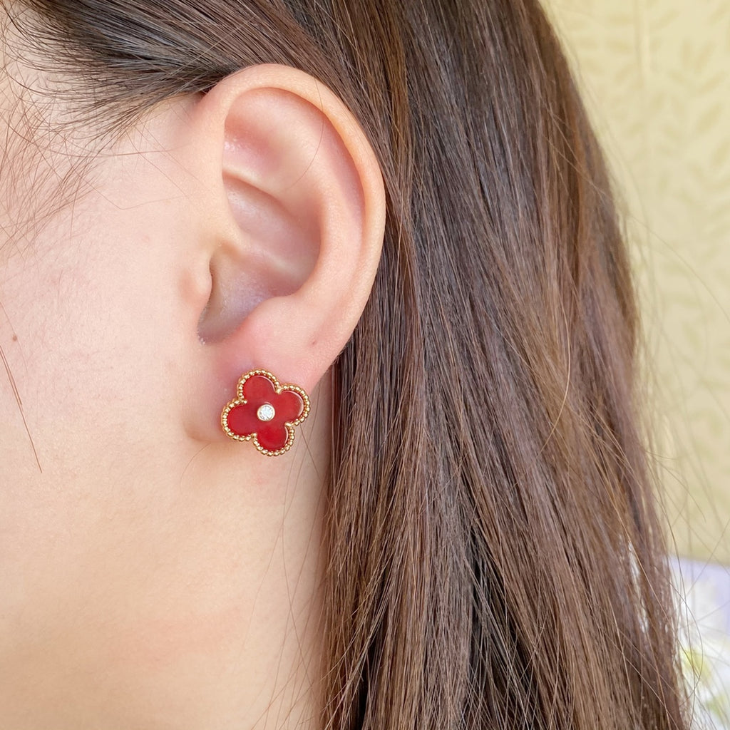 Clover-shaped stud earrings with gold-tone frame and red center on a wearer’s ear