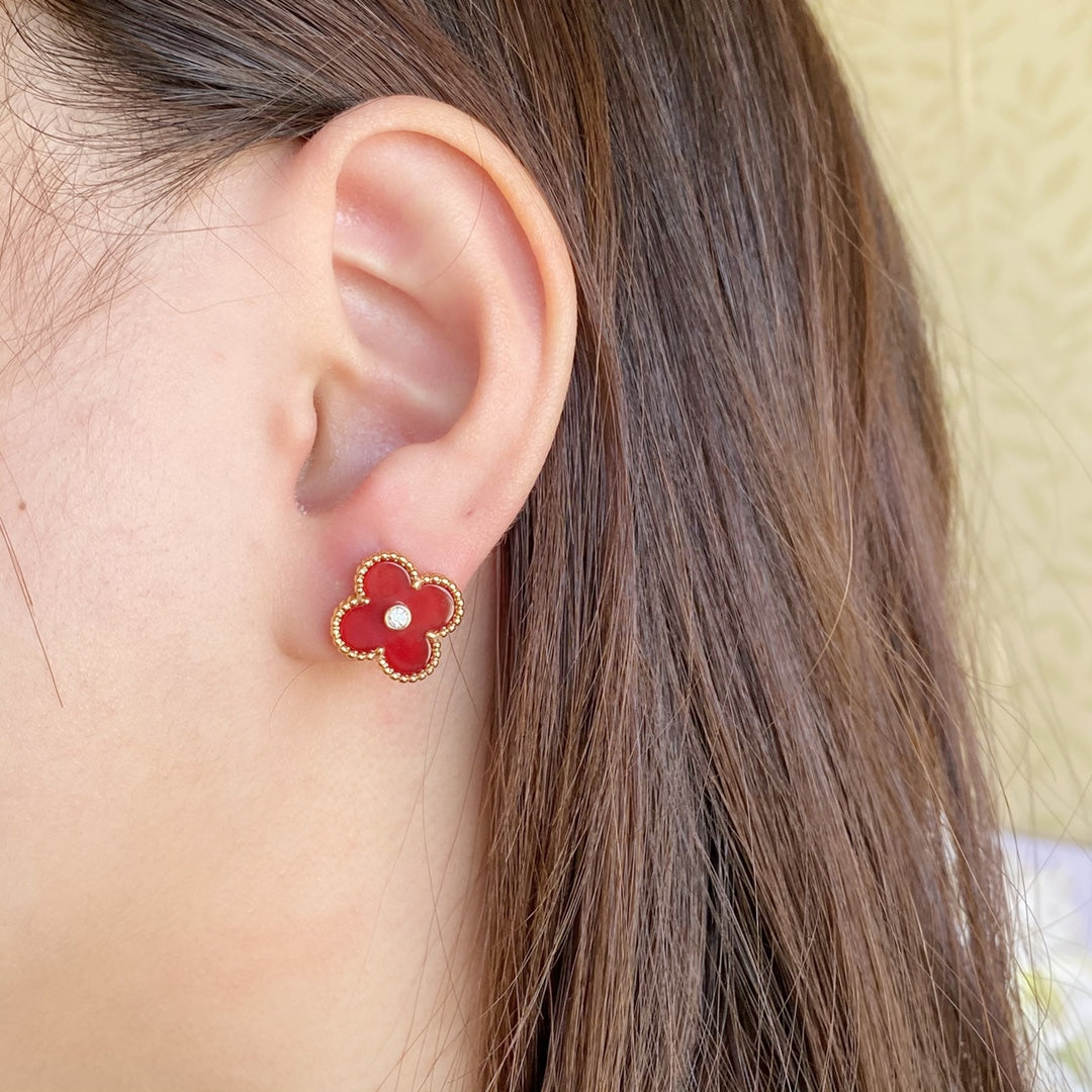 Clover-shaped stud earrings with gold-tone frame and red center on a wearer’s ear