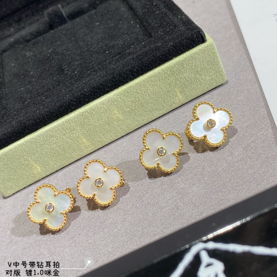 Clover-shaped stud earrings with gold-tone frames in white on a display tray