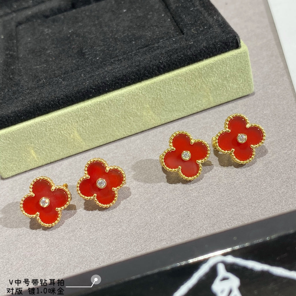 Clover-shaped stud earrings with gold-tone frames in red on a display tray