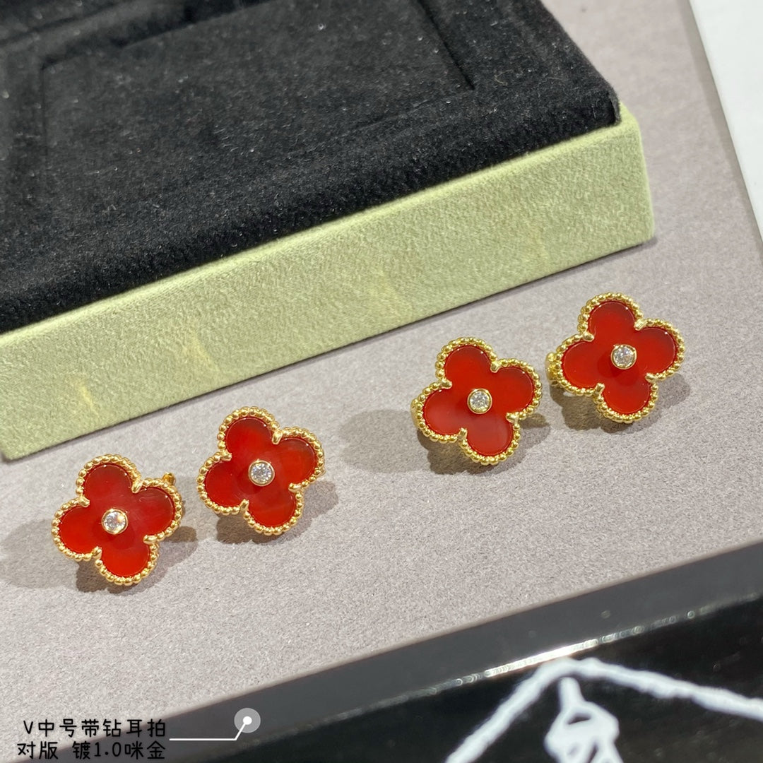 Clover-shaped stud earrings with gold-tone frames in red on a display tray