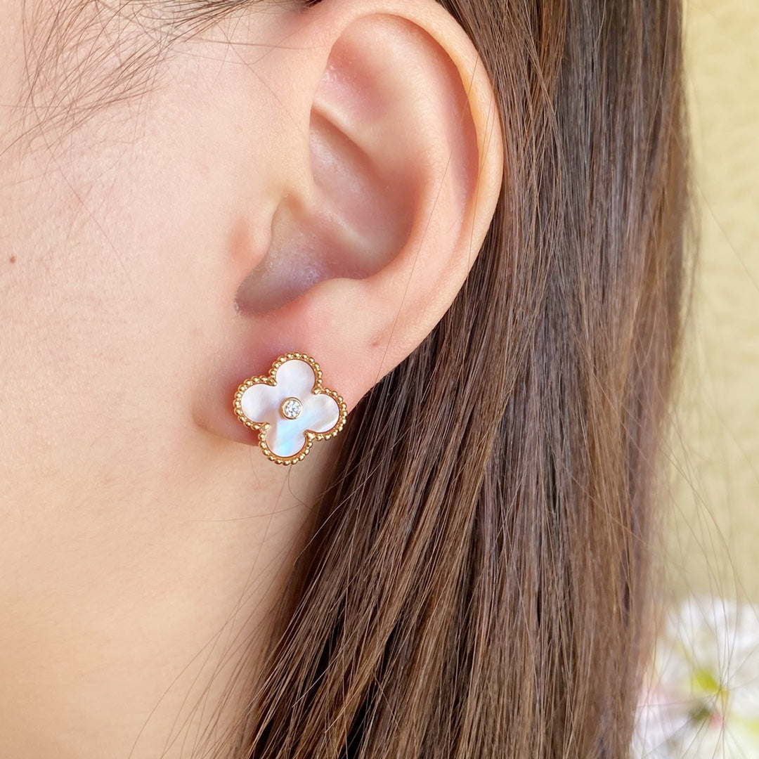 Gold clover stud earrings with white enamel petals and a round clear center stone on ear