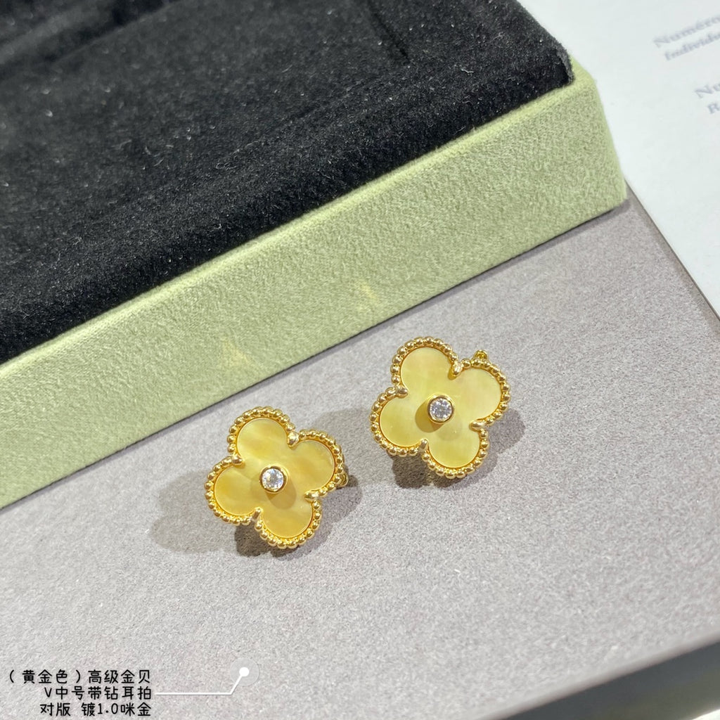 Gold clover stud earrings with clear stones, pair shown on a light display surface.