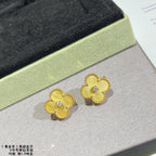 Gold clover stud earrings with clear stones, pair shown on a light display surface.