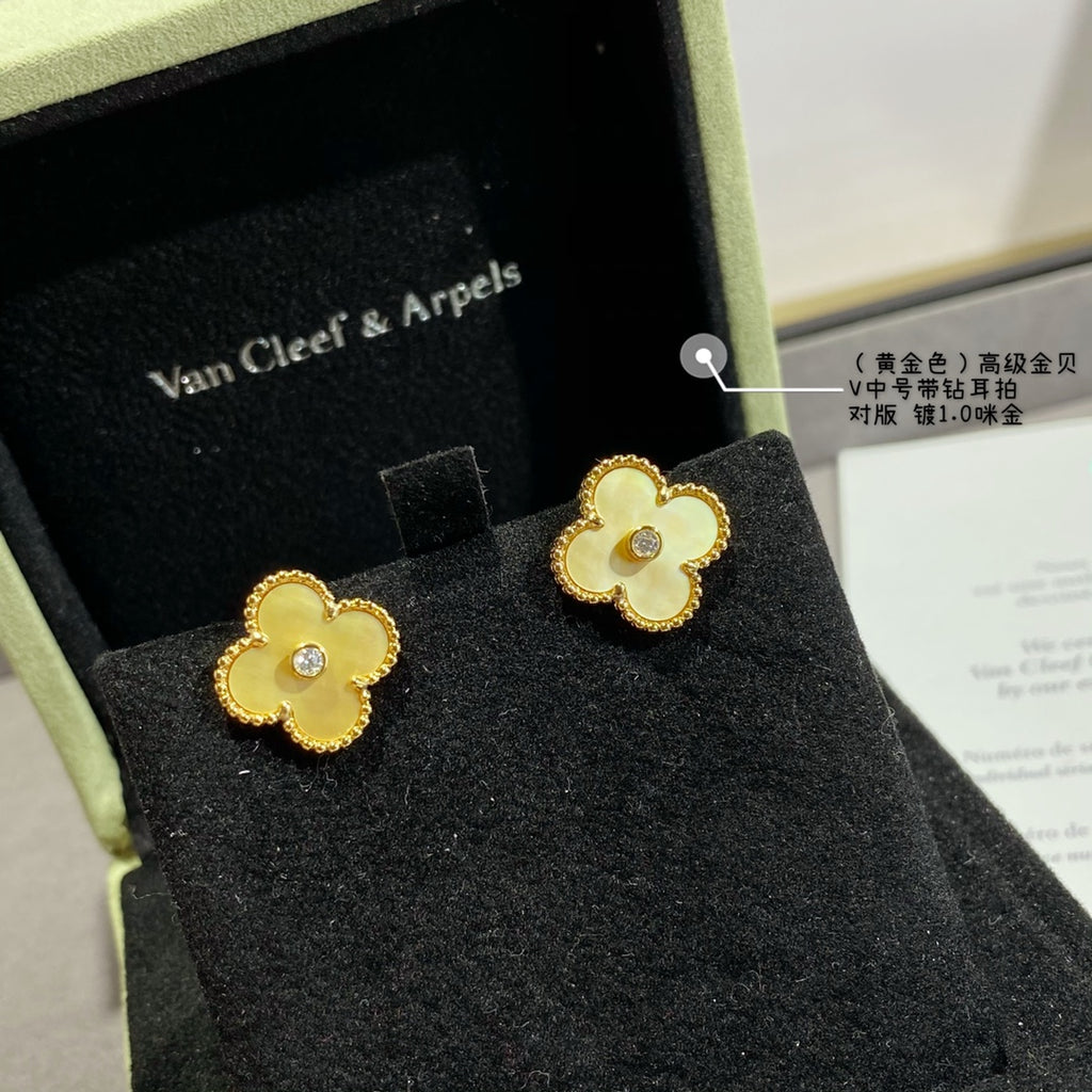 Gold clover stud earrings with small clear stone centers, on display in a jewelry box.