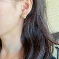 Gold clover stud earrings with clear center stones, worn at the ear.