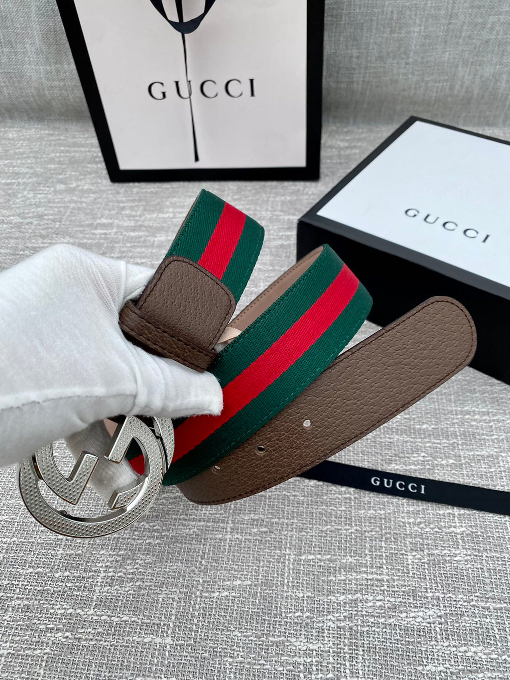 Brown leather Gucci belt with silver-tone GG buckle and green/red web stripe held by hand
