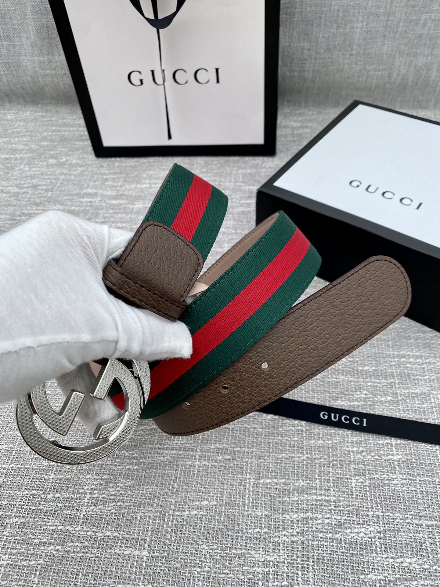 Brown leather Gucci belt with silver-tone GG buckle and green/red web stripe held by hand