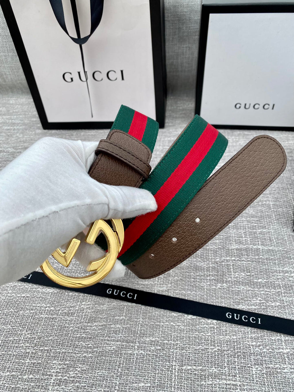 Gucci belt with brown leather strap, gold double G buckle, and green-red stripe web detail.