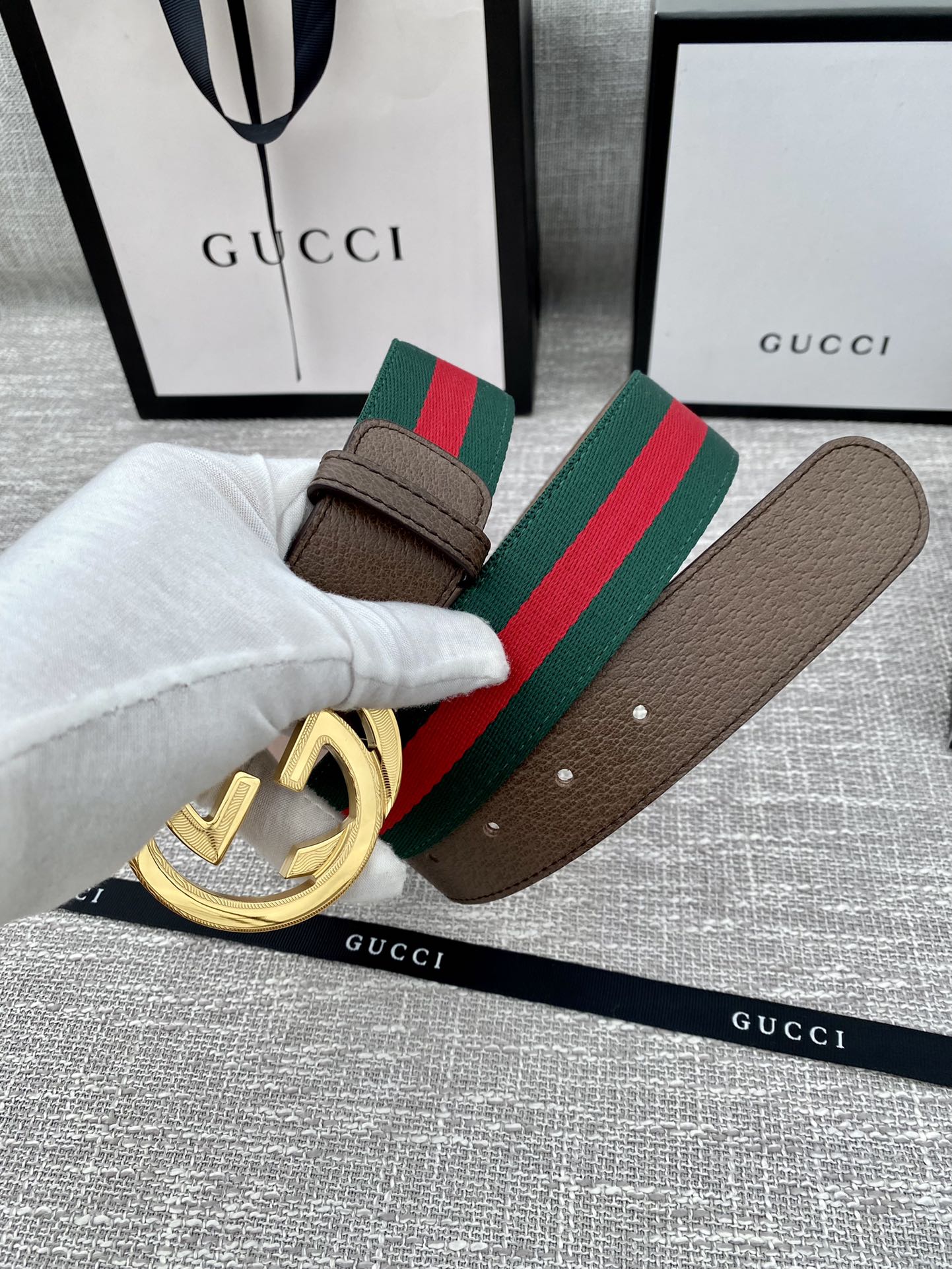 Gucci belt with brown leather strap, gold double G buckle, and green-red stripe web detail.