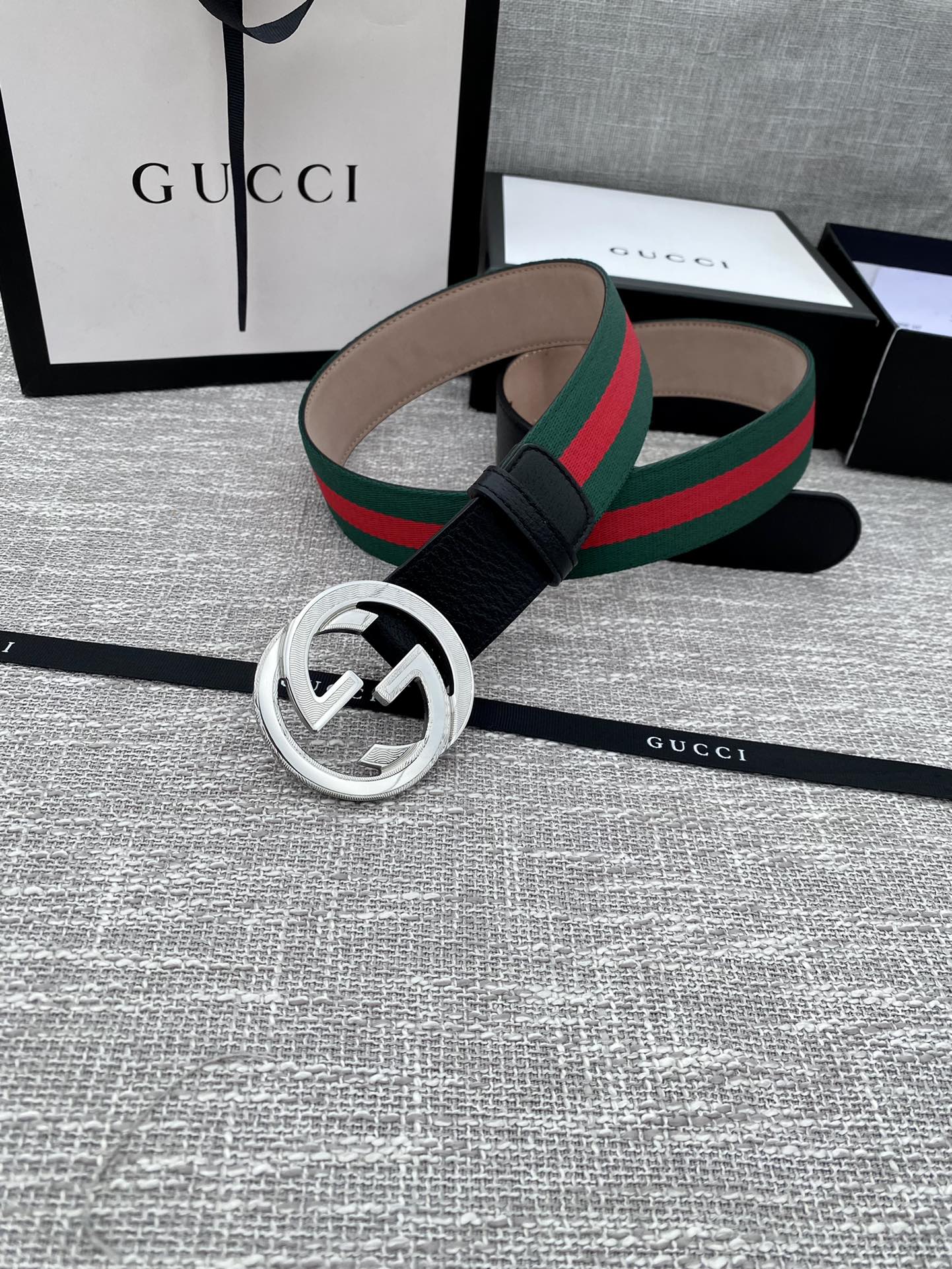 Black leather belt with silver-tone GG buckle and green-red web stripe, laid out