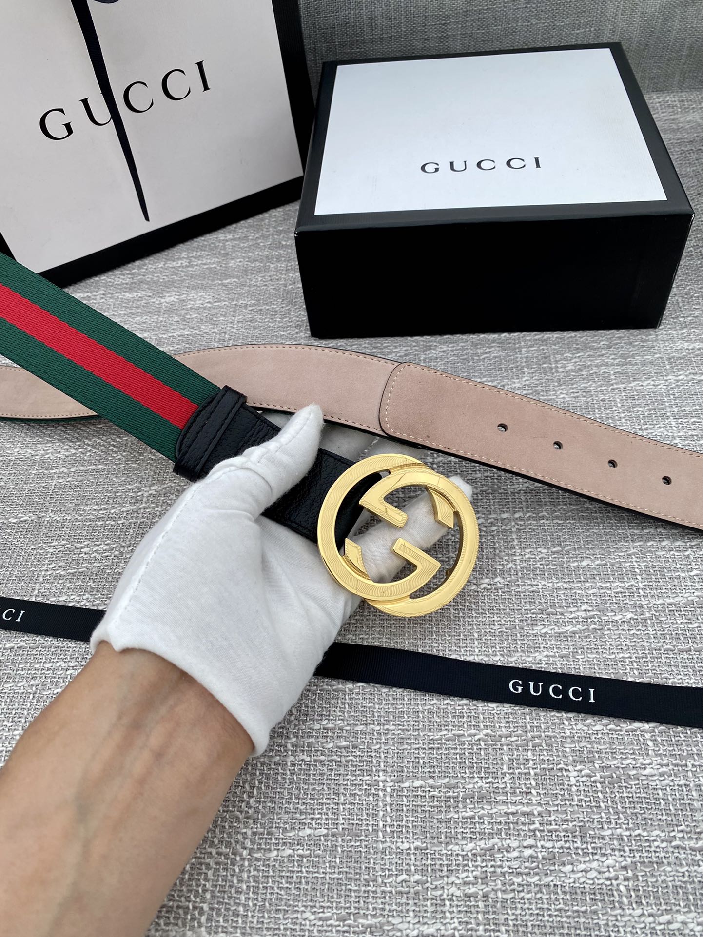 Black leather belt with gold-tone GG buckle in hand, green-red web stripe