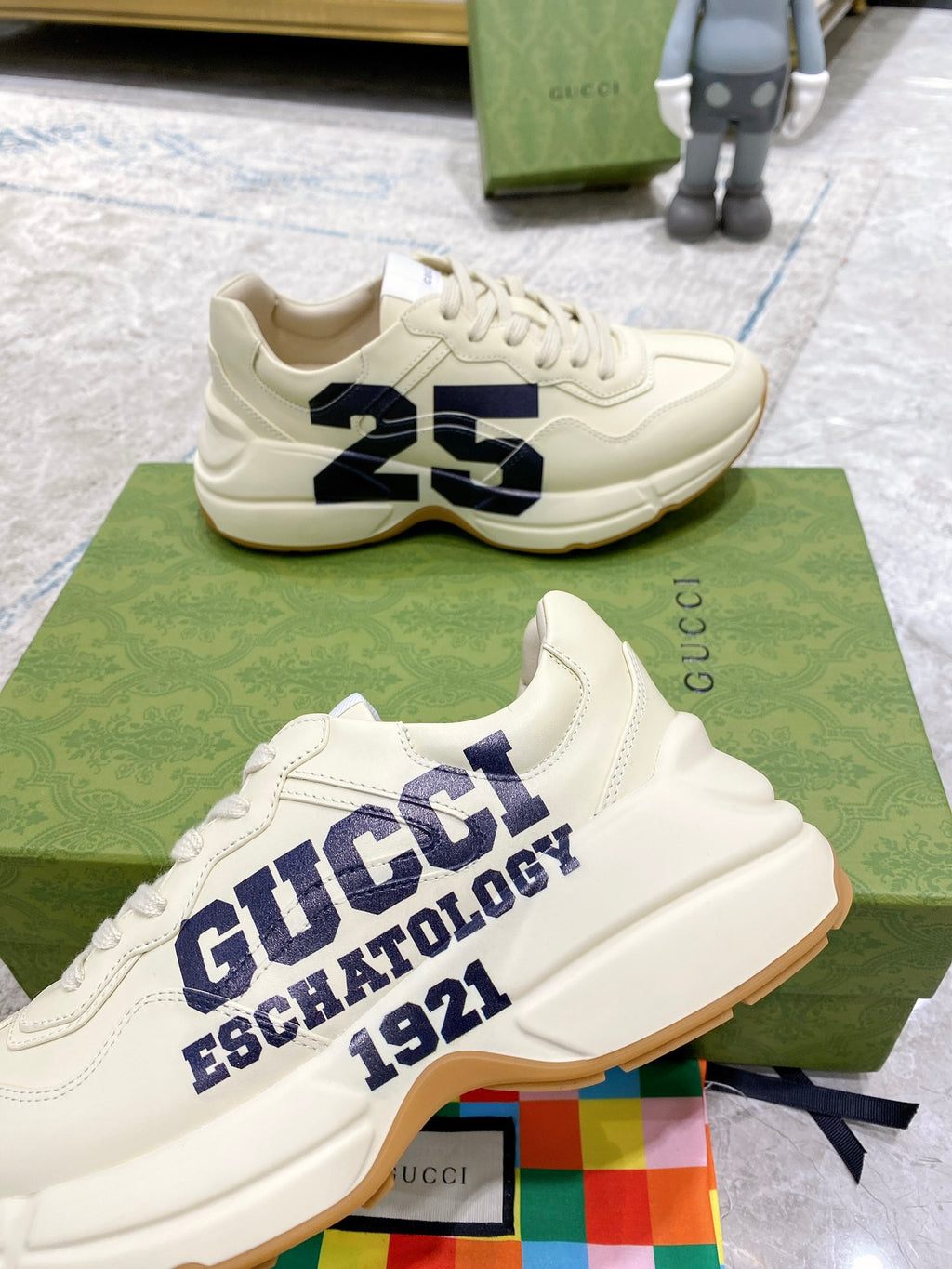 Cream low-top sneakers with navy "GUCCI ESCHATOLOGY 1921" lettering