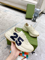 Cream sneakers with navy 25 logo, held above green shoebox