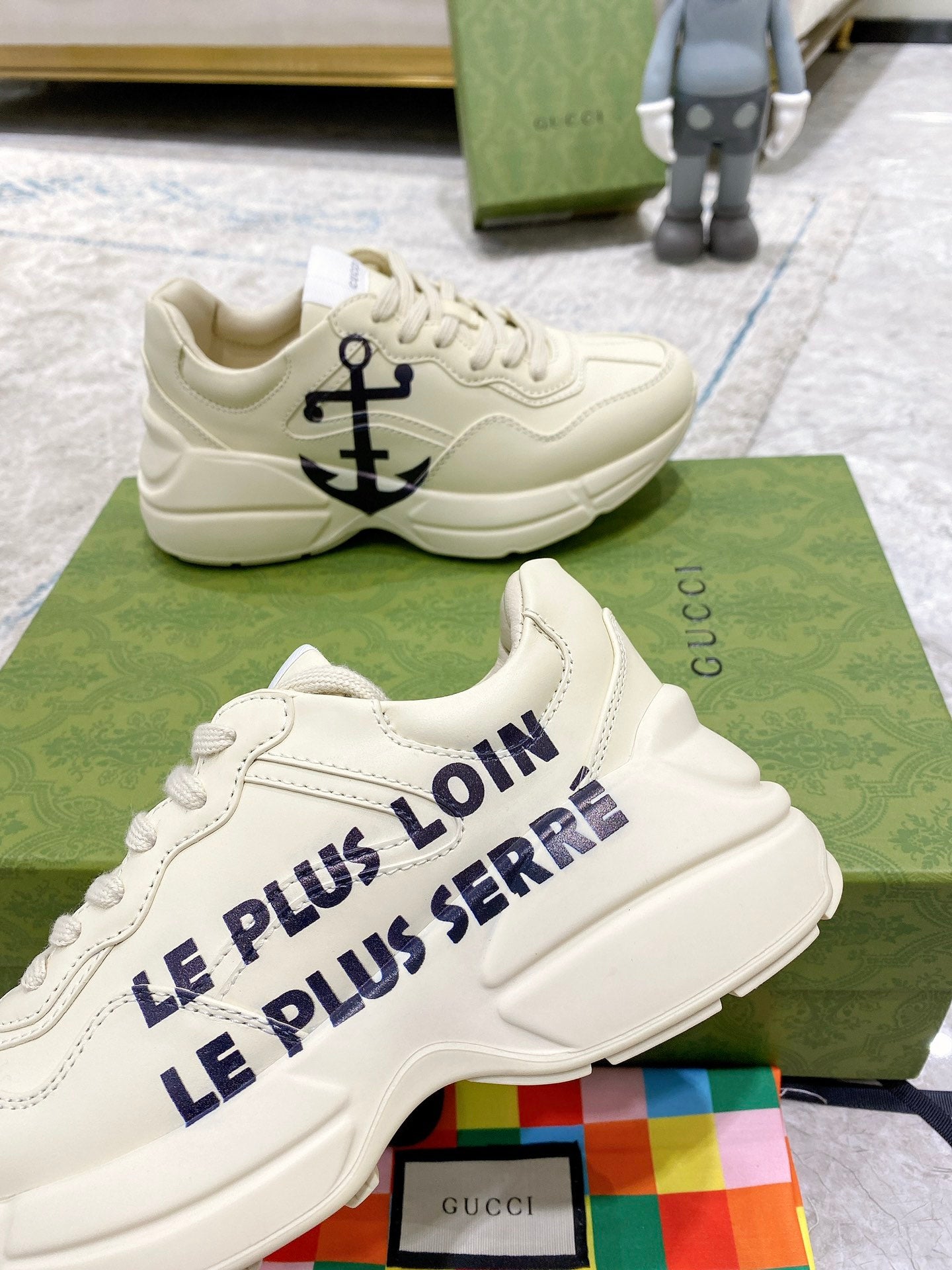 Cream Gucci sneakers with blue anchor logo on side, angled view on green box.