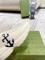 Cream Gucci sneakers side view with blue anchor emblem and textured sole edge.