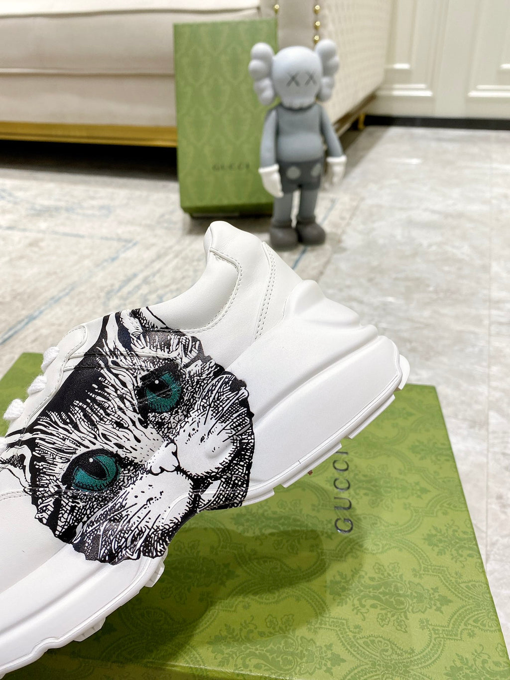 White Gucci unisex sneaker close-up with cat-face graphic featuring green eyes.