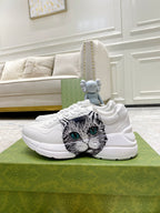 White Gucci unisex sneakers with cat-face print and green eyes on side panel.