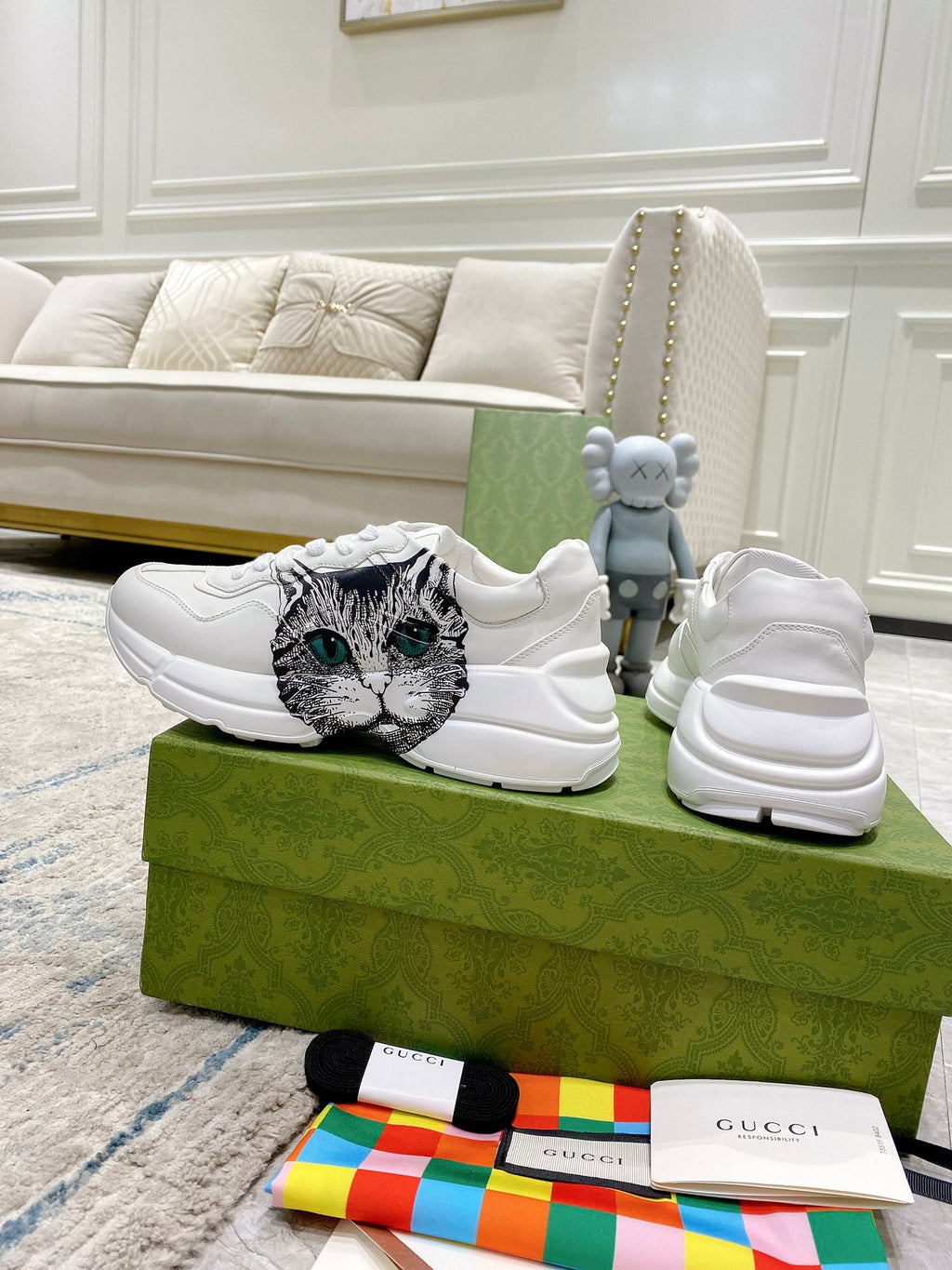 White Gucci unisex sneakers on green box, left shoe shows cat-face graphic; right spare.