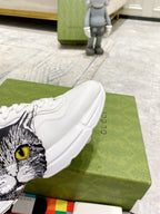 White Gucci unisex sneaker close-up showing cat-face graphic on side and heel tab.