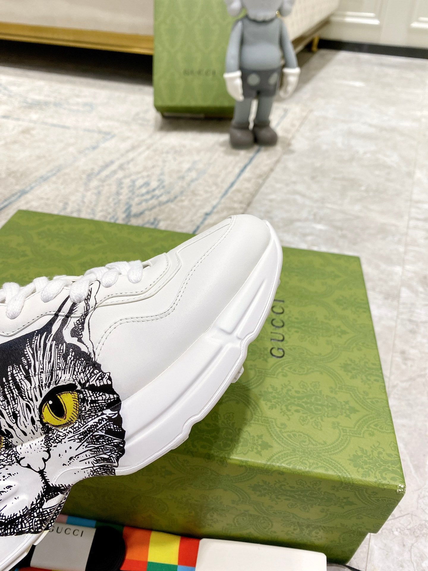 White Gucci unisex sneaker close-up showing cat-face graphic on side and heel tab.