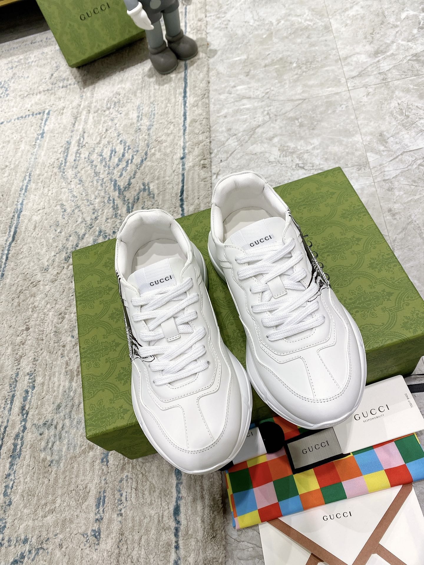 White Gucci unisex sneakers, front view with lace-up detailing and side cat graphic.