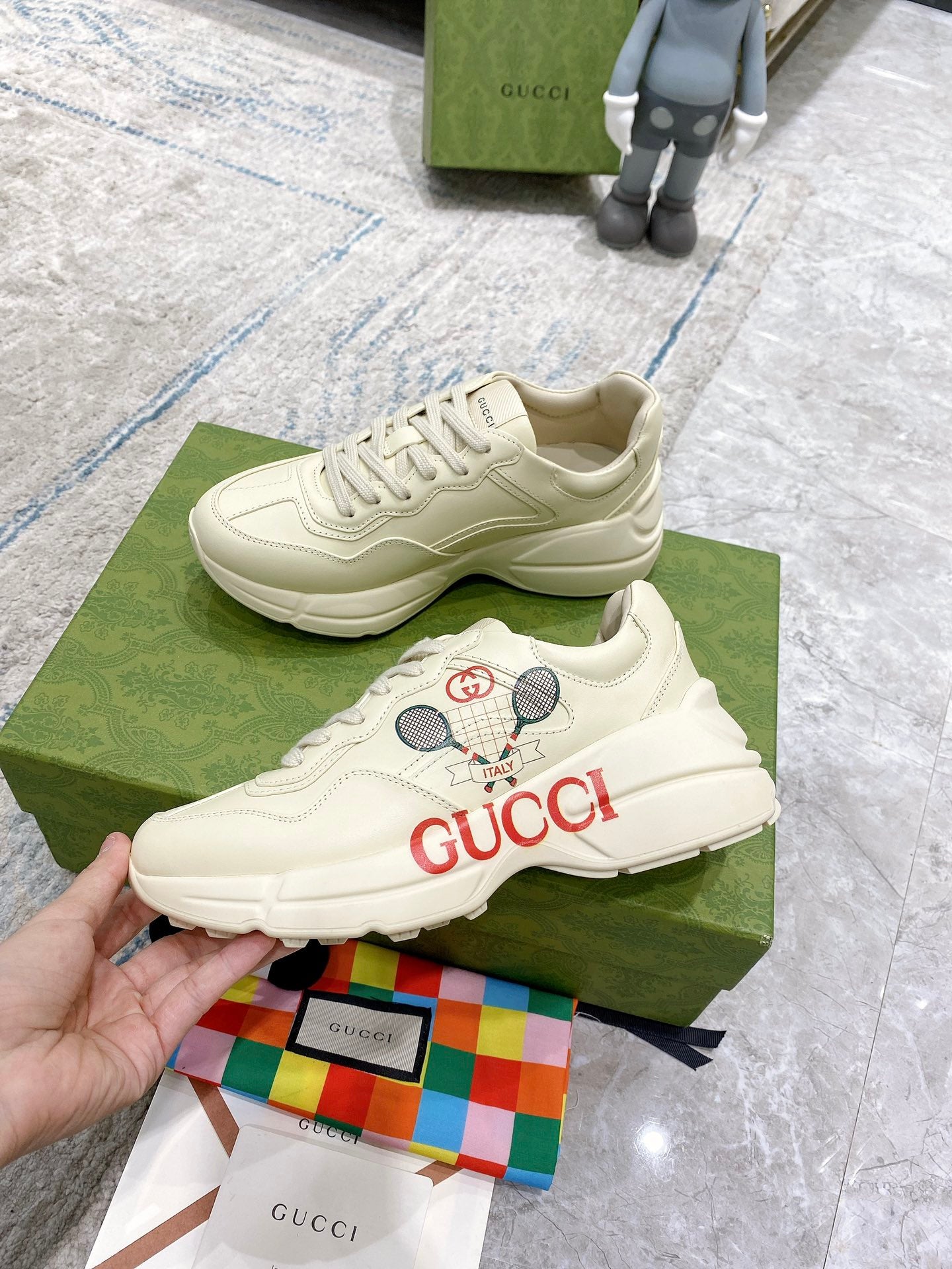 Cream unisex Gucci sneakers on green box, lace-up with tennis graphic