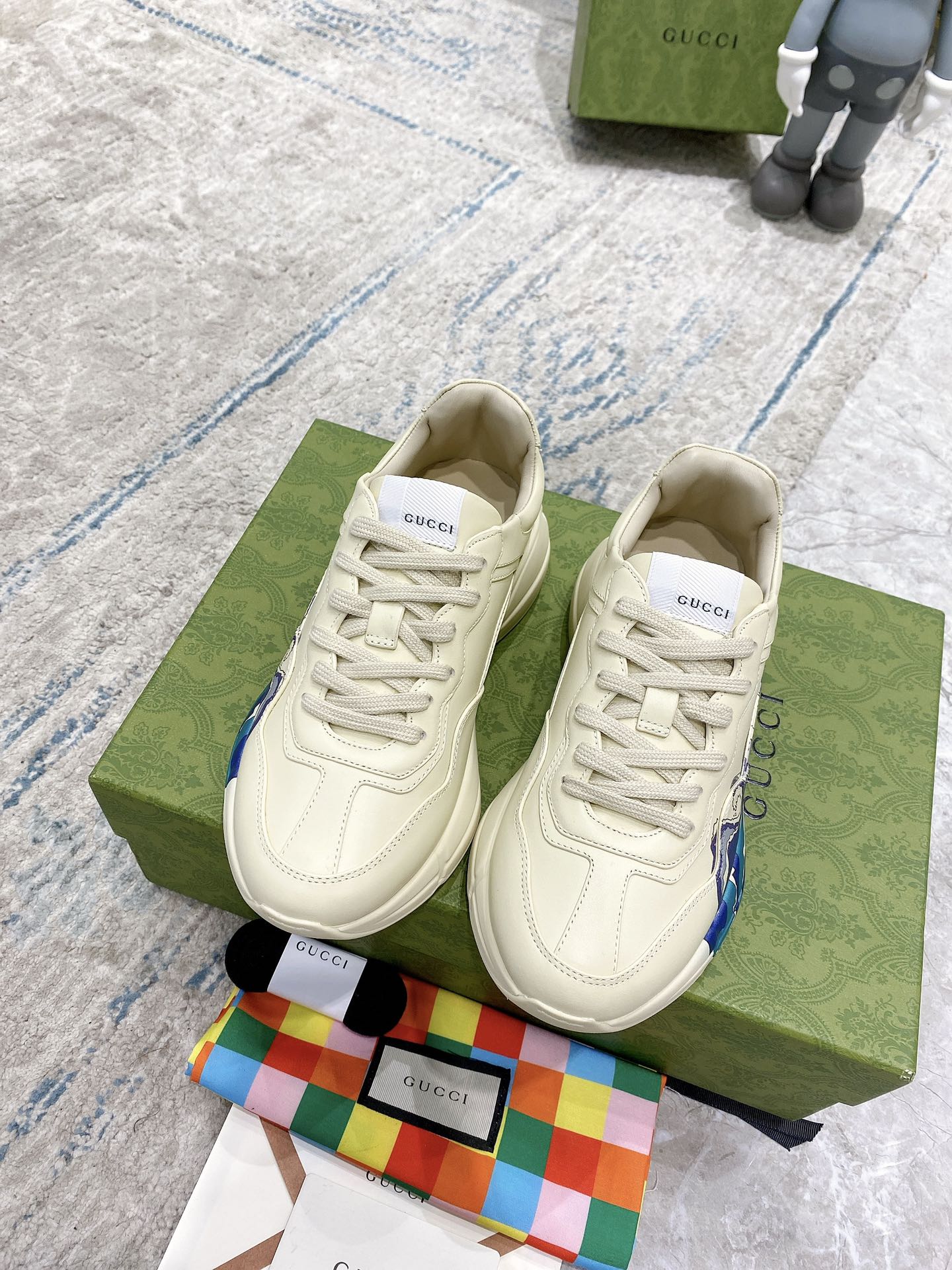Cream/white Gucci unisex sneakers on green box, lace-up with blue wave side panel