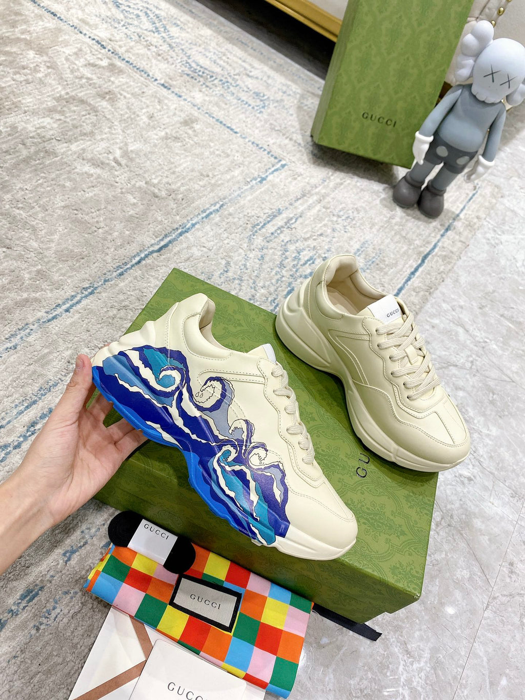White Gucci unisex sneakers with blue wave side graphic, displayed on green box