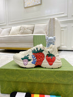Gucci unisex sneakers on a green box: cream lace-up with strawberry and flower patches.