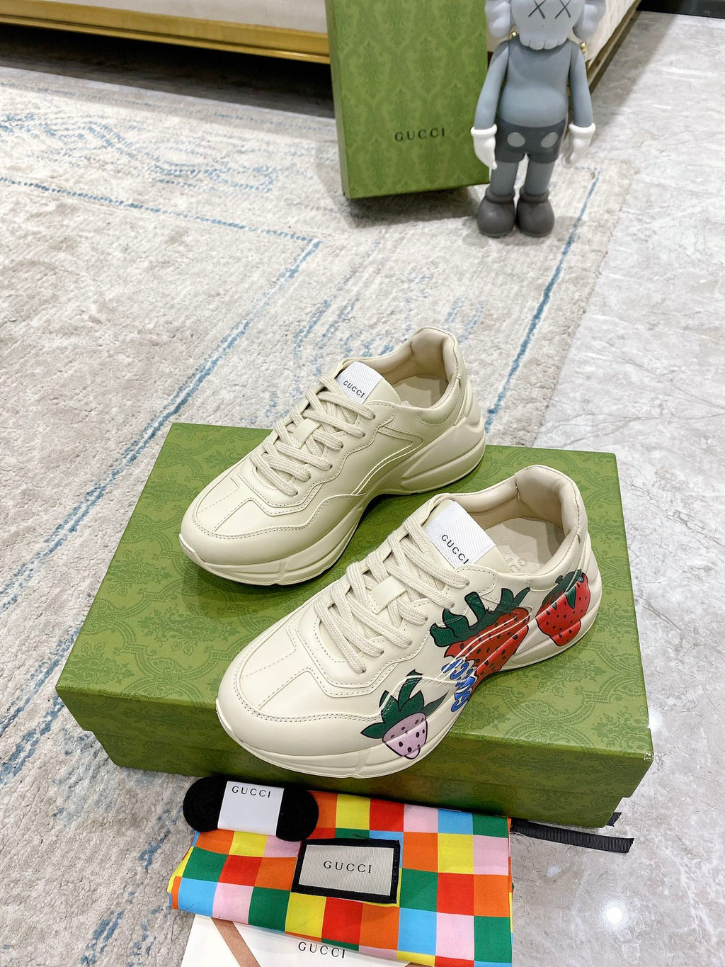 Gucci unisex sneakers on box: cream lace-up with strawberry side artwork and patterned tongue.