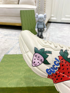 Gucci unisex sneakers side view: cream lace-up with strawberry graphic and blue swoosh text.