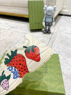 Gucci unisex sneakers close-up: cream canvas with strawberry graphic and blue lettering detail.