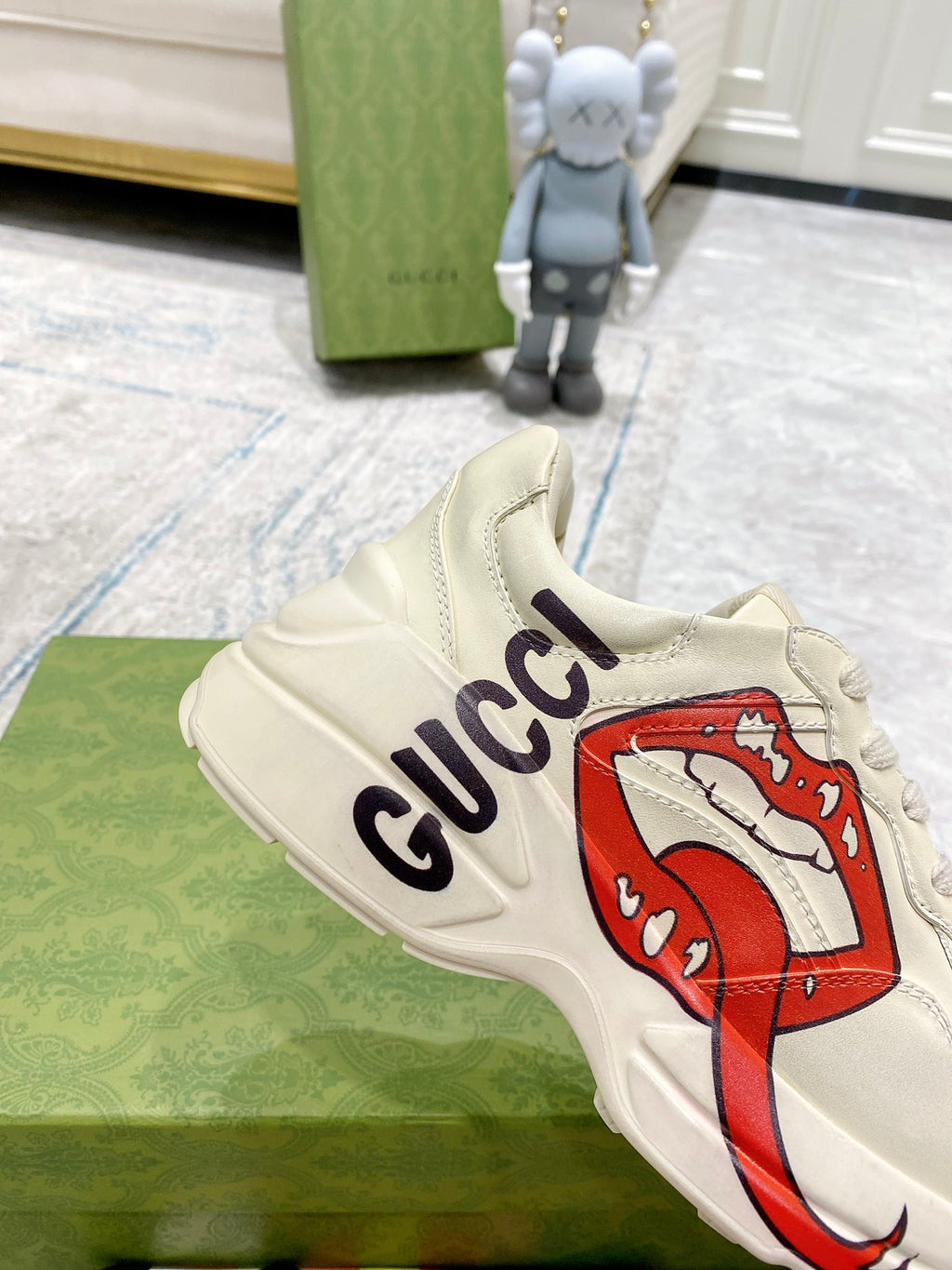 Light-cream Gucci unisex sneaker close-up with red lip graphic and navy Gucci logo