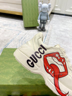 Light-cream Gucci unisex sneaker close-up with red lip graphic and navy Gucci logo