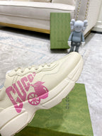 Cream Gucci sneaker side view with pink logo print and lace-up front on display.