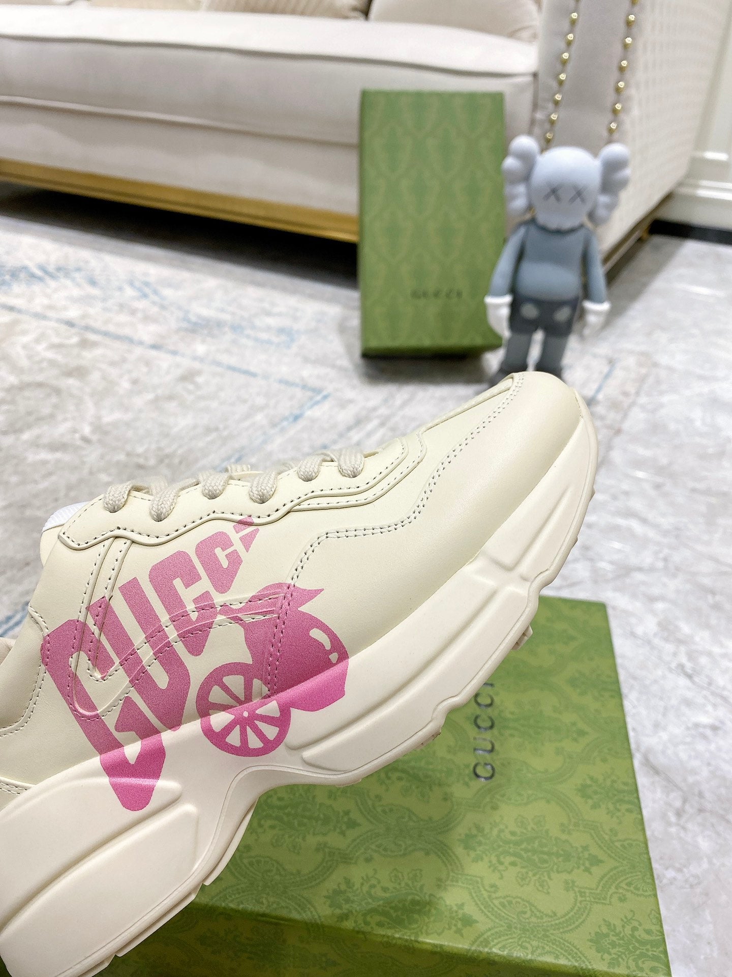 Cream Gucci sneaker side view with pink logo print and lace-up front on display.