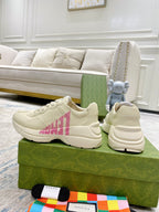 Cream Gucci sneakers with pink logo detail, stitched overlays and lace-up design.