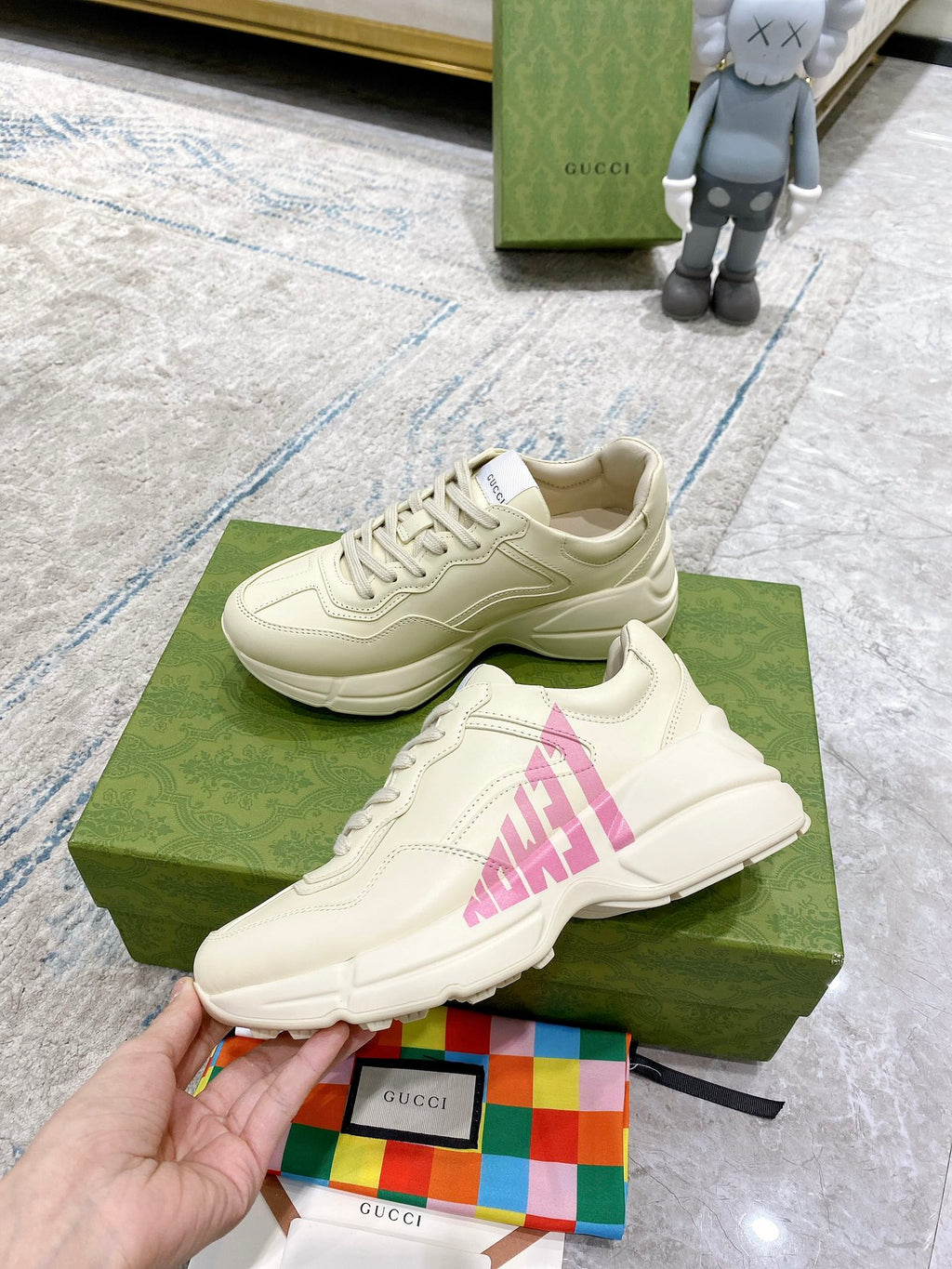 Cream Gucci sneakers with pink logo graphic, shown with laces and thick sole.