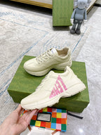 Cream Gucci sneakers with pink logo graphic, shown with laces and thick sole.