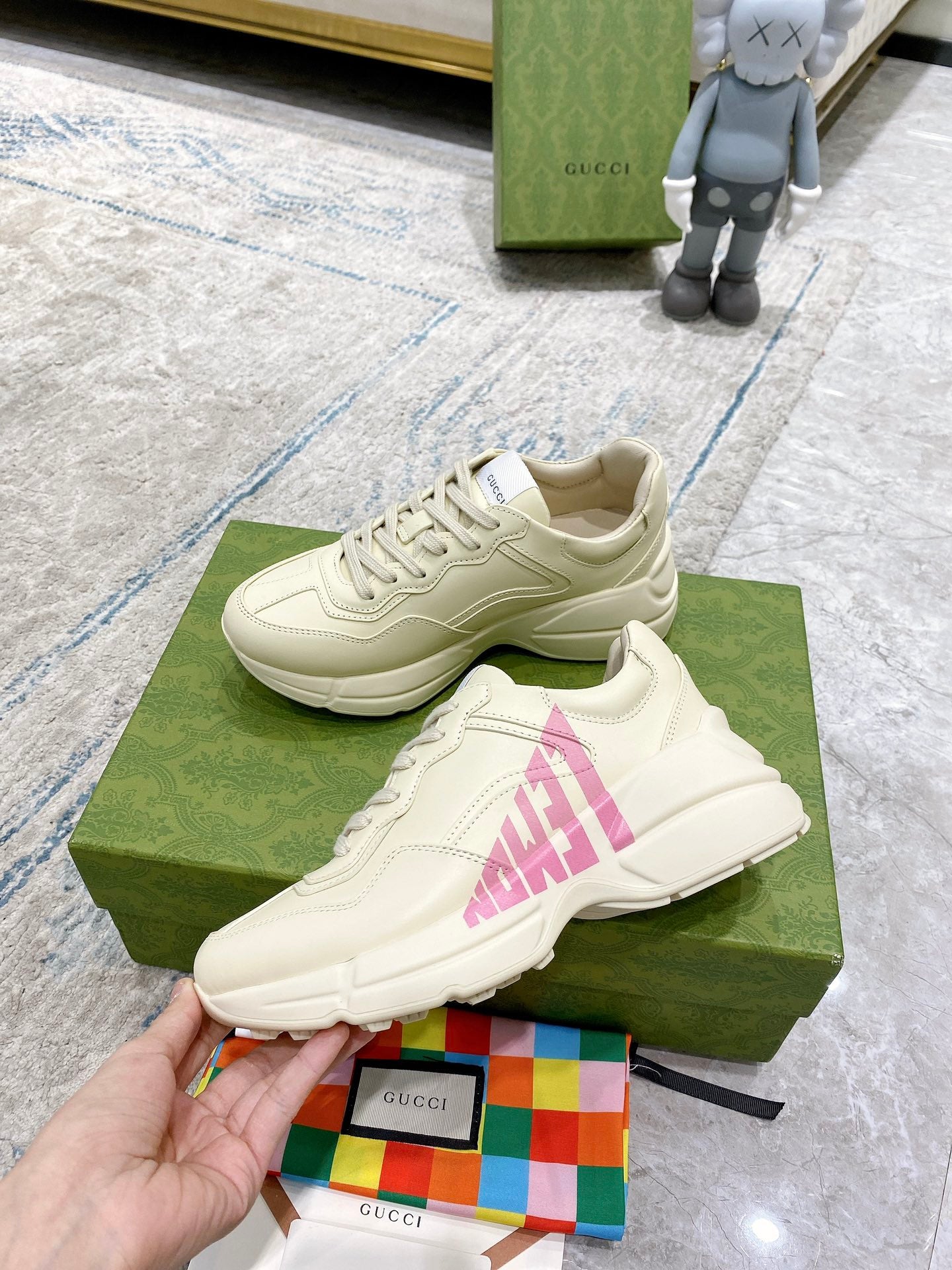 Cream Gucci sneakers with pink logo graphic, shown with laces and thick sole.