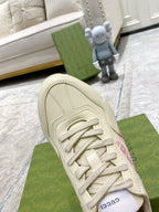 Cream Gucci sneaker upper detail: lace-up with stitched panels and pink logo on side.