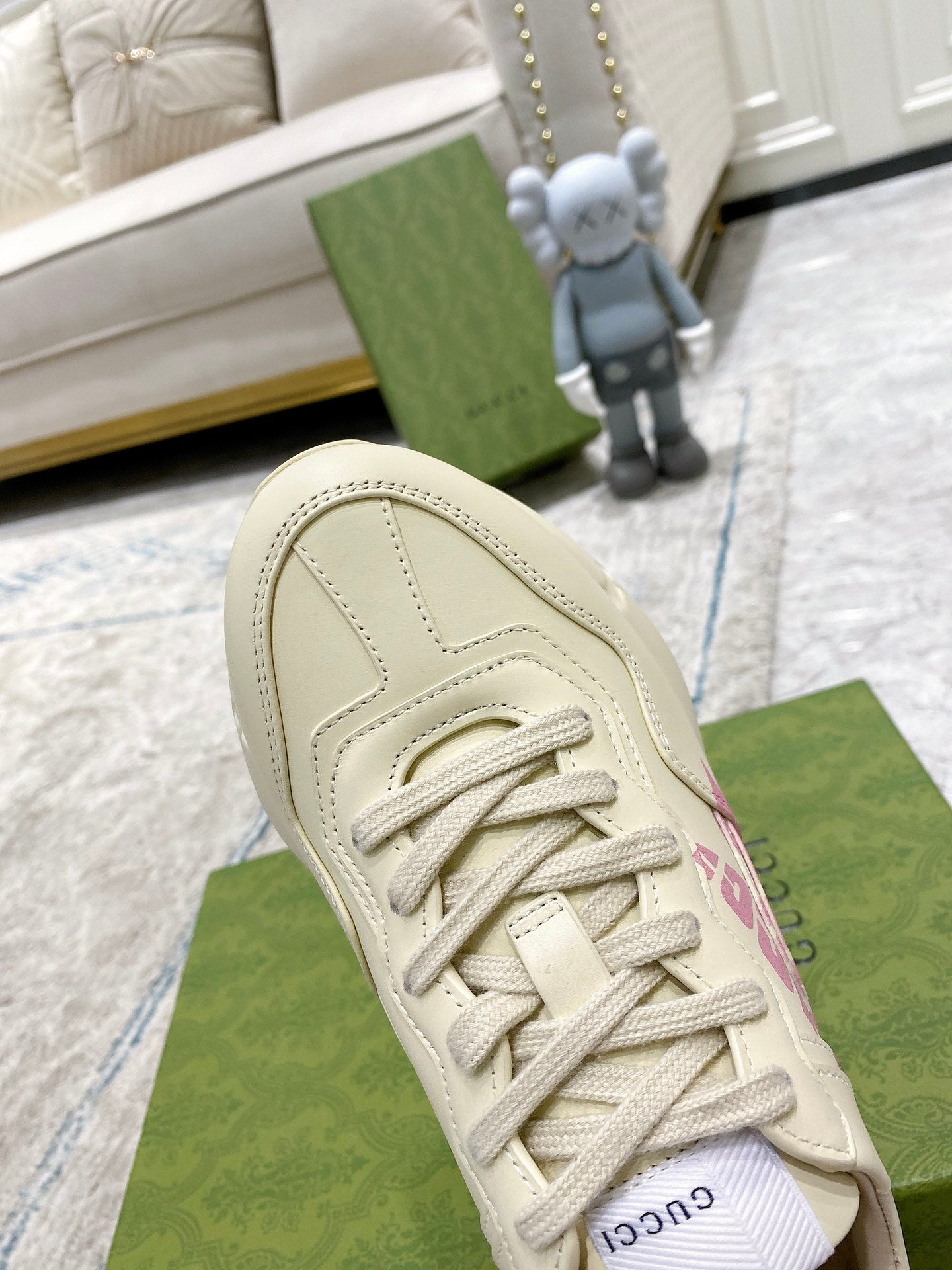 Cream Gucci sneaker upper detail: lace-up with stitched panels and pink logo on side.