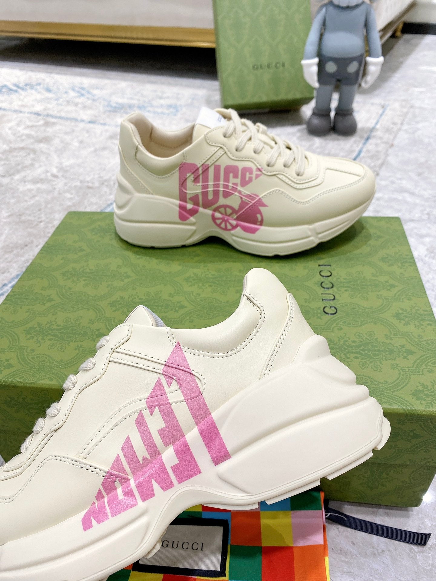 Cream Gucci sneakers with pink logo graphic, close side view with stitched trim.