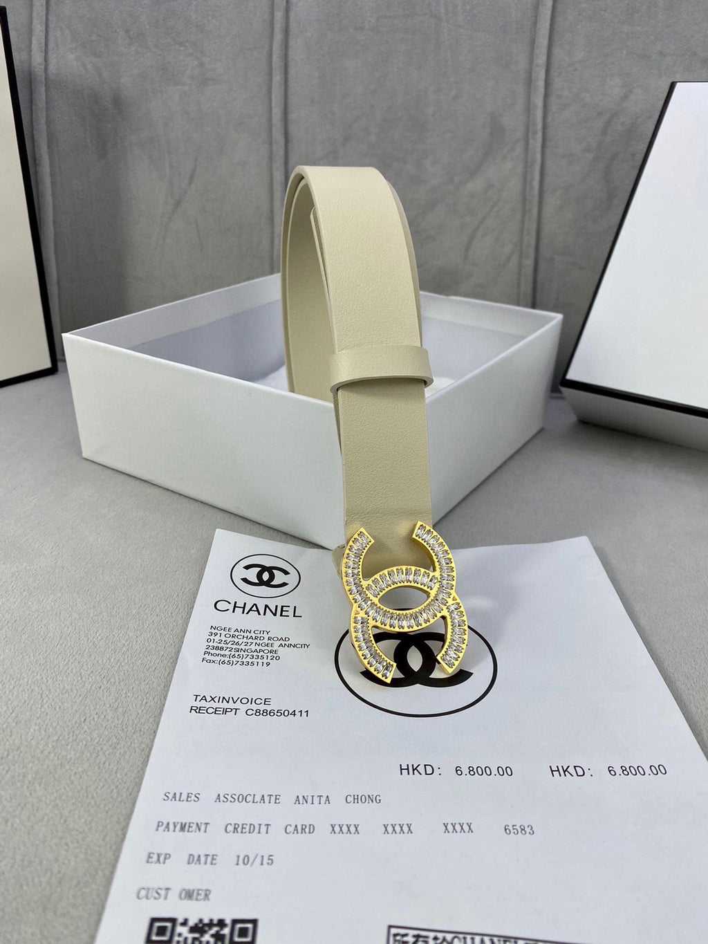Beige leather belt with Chanel CC rhinestone buckle standing in a white box