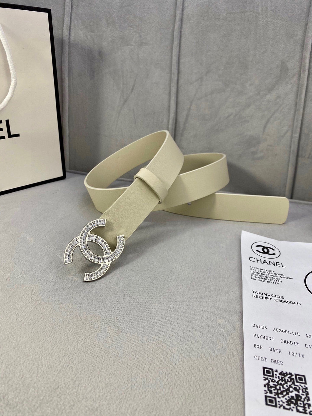 Beige leather belt with Chanel CC rhinestone buckle beside a Chanel document card