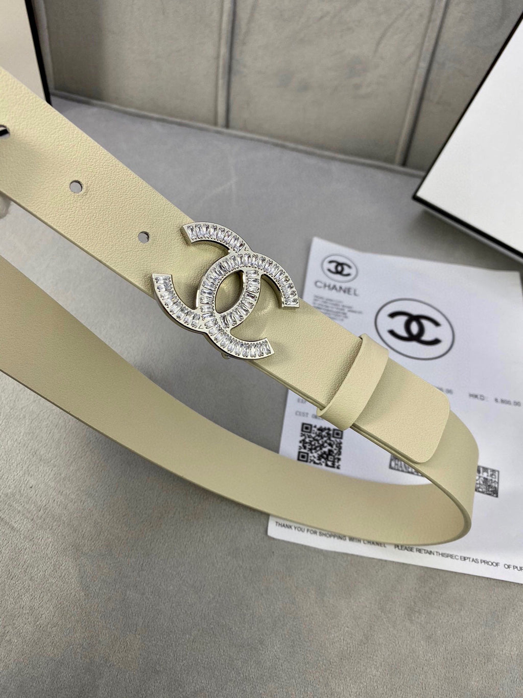 Beige leather belt with Chanel CC rhinestone buckle laid flat with holes visible