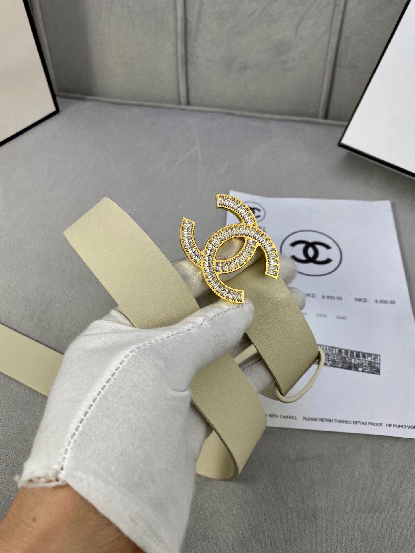 Beige leather belt with Chanel CC rhinestone buckle, partly held by a glove